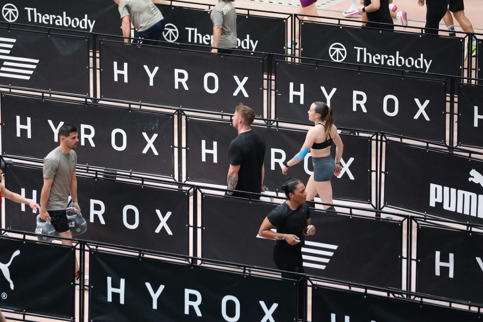 Hyrox afişleriyle çevrili alanda antrenman yapan kişiler